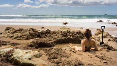 nieuw-zeeland_noordereiland_coromandel_hot-water-beach_vrouw_zee_strand_schep_shutterstock_554194648