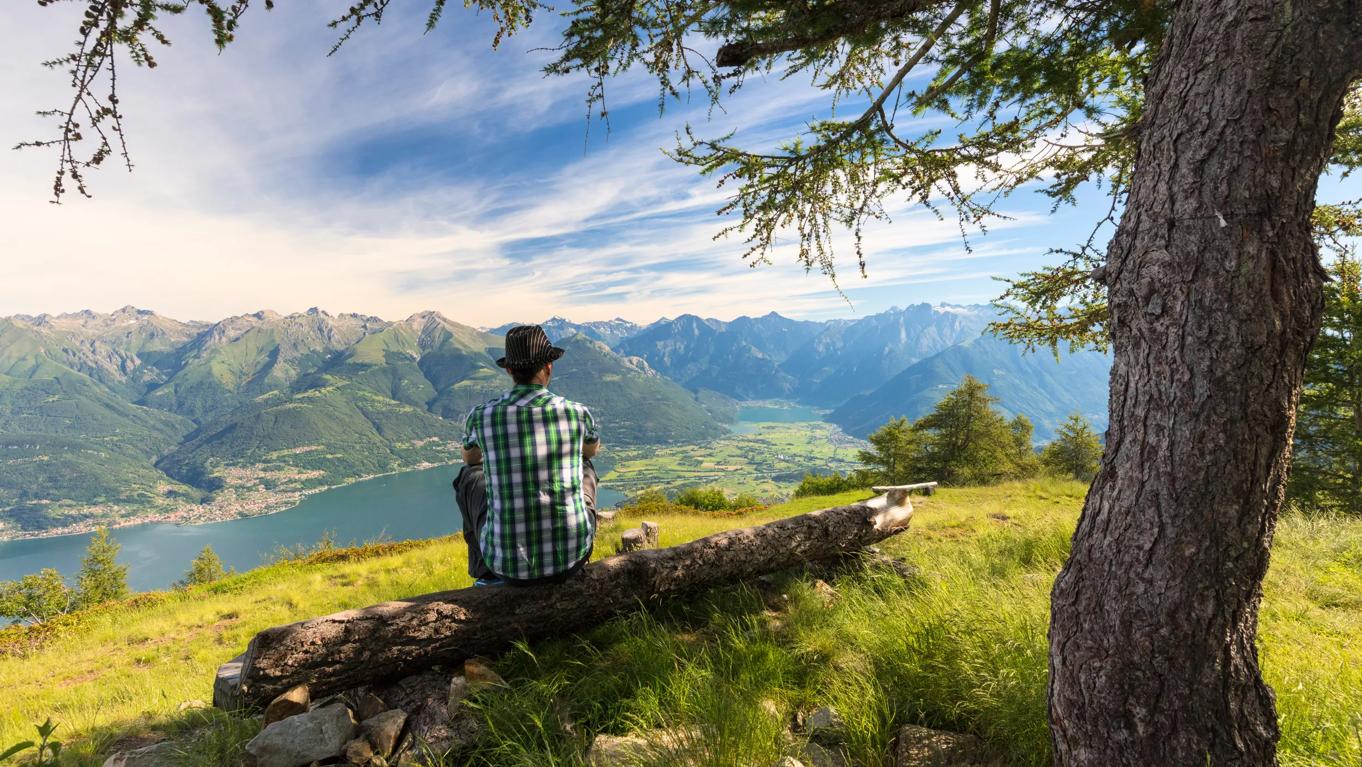 Een man die op een boomstronk zit en het Lecco uitzicht bewonderd