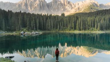Young Caucasian woman standing and looking at  Lago di Carezza in Dolomites