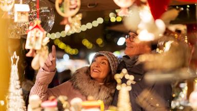 shopping, winter holidays and people concept - happy senior couple at christmas market souvenir shop on town hall square in tallinn, estonia