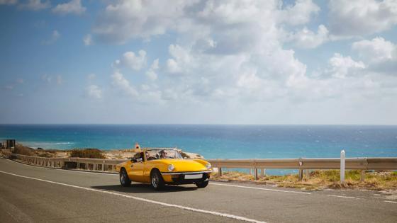 Young hipster women on summer holidays driving yellow vintage convertible car by the sea