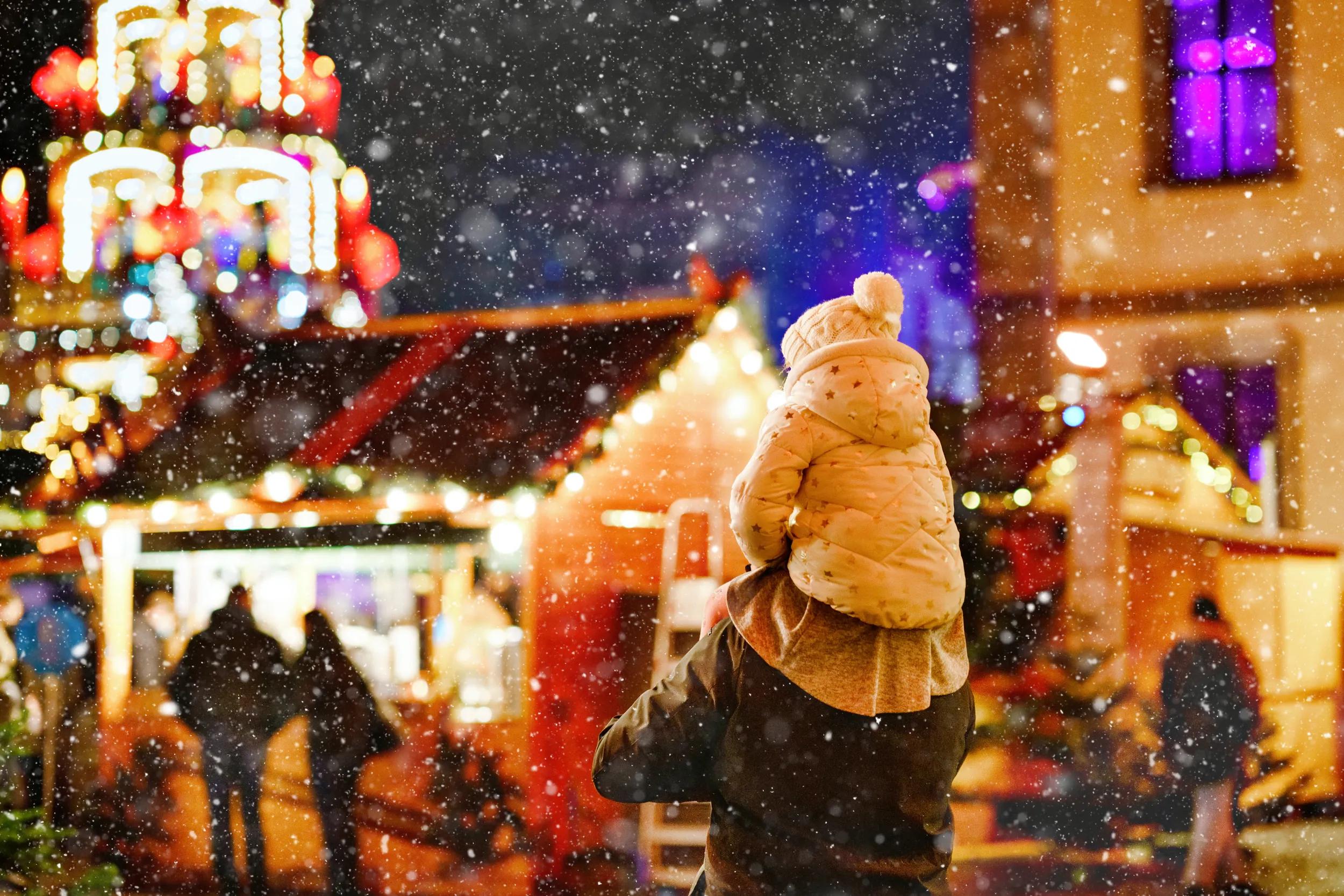 Little preschool girl sitting on shoulder of father on Christmas market in Germany. Happy toddler child and man observing traditional decorated pyramid. Happy family, bonding, love. Family xmas time