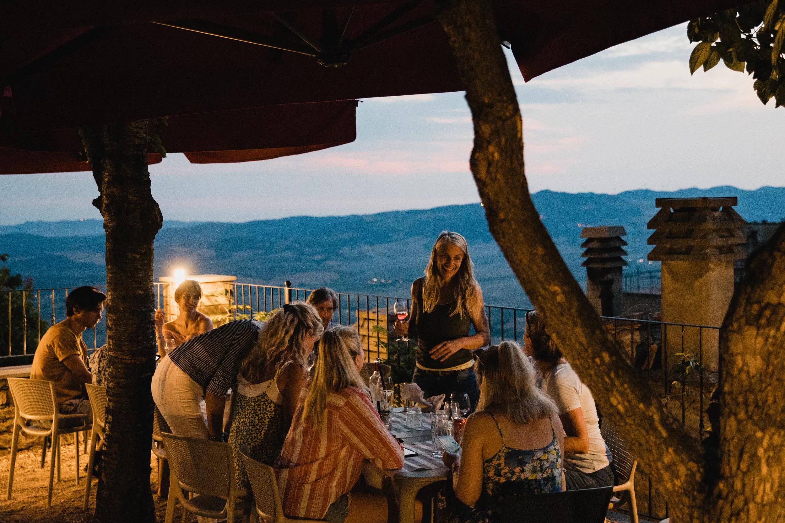 Large group of people enjoying an Italian meal together on top of a rooftop restaurant.