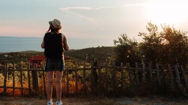Young woman with a backpack enjoying sunset and the view from the top of a hill in Greece