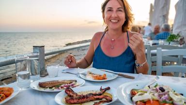 Middle age Greek woman is sitting in a restaurant (taverna) near sea and happy with wonderful and delicious Greek meal and Ouzo in city of Alexandroupoli. She's looking to camera.