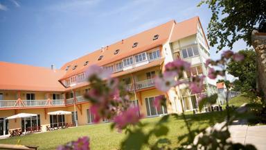 Aussenansicht mit Blumen im Sommer vom JUFA Hotel Nördlingen. Der Ort für kinderfreundlichen und erlebnisreichen Urlaub für die ganze Familie.