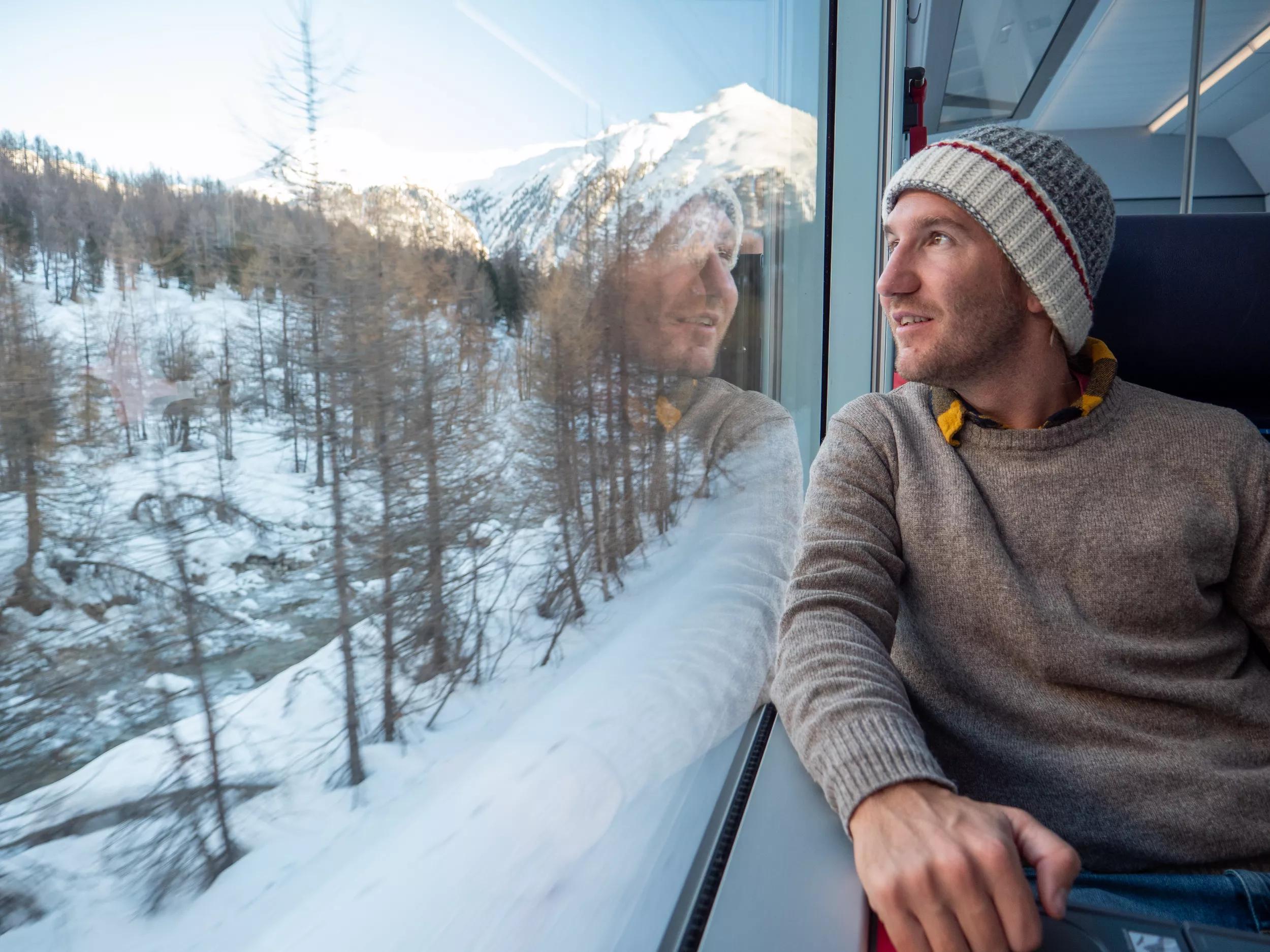 Travel man tourist in train visiting Switzerland enjoying beautiful panorama through window. People travel enjoyment eco tourism concept. Man discovering the Swiss Alps by train