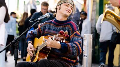 Young man with long hair and a headband playing guitar with a passion expression in the street in Galway