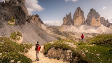 Two women hiking at Tre Cime di Lavaredo, Dolomites Alps, Italy. Blue Sky, wildflowers.