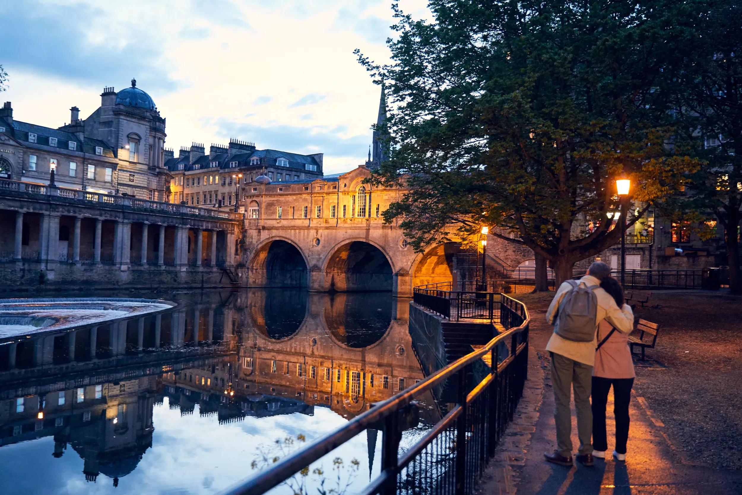 A couple strolling by Pulteney Bridge and the River Avon in Bath, England.