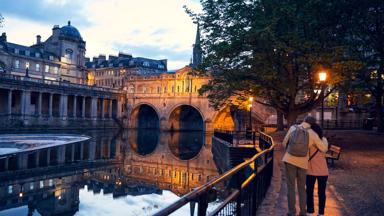 A couple strolling by Pulteney Bridge and the River Avon in Bath, England.