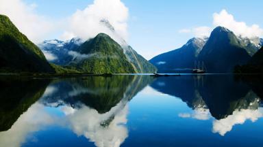 nieuw-zeeland_zuidereiland_fiordland-national-park_milford-sound_boot_water_fjorden_gebergte_besneeuwde-bergtop_weerspiegeling