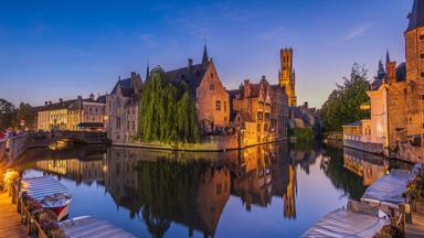 Canal of the Rosary Quay in the Hanseatic city of Bruges in the evening. Reflection on the water surface of the historic buildings. Belfry of the old town and historic guild houses and merchant houses