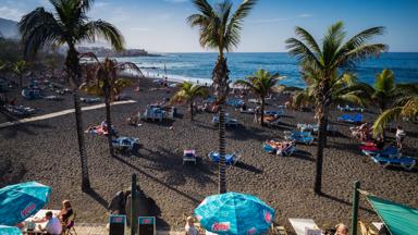 spanje_canarische-eilanden_tenerife_puerto-de-la-cruise_lava-strand_palmbomen_terras_strandbedjes_zee_toeristen_getty-586283165