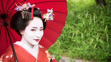 Young woman in traditional maiko costume smiling, white make up on face and flowers in hair