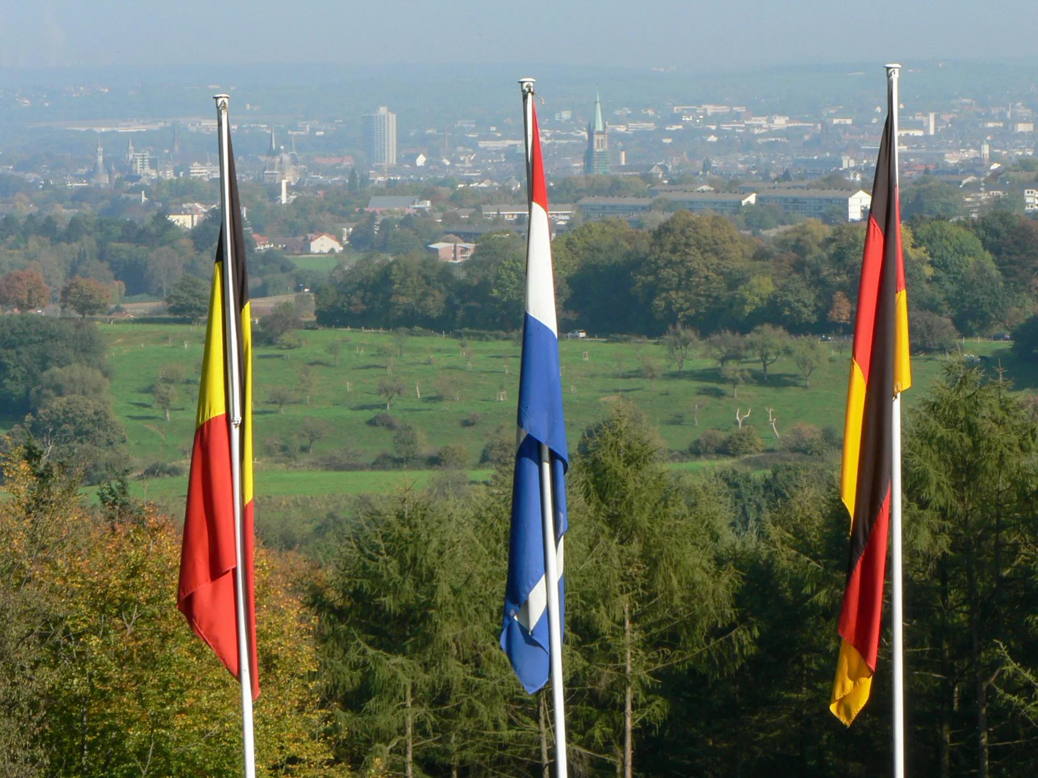 Detail of flags of Belgium, Netherlands and Germany from the tripoint ('Drielandepunt' in Dutch, 'Trois Frontières' in French, and 'Dreiländereck' in German), where the borders of the three countries meet. Forest and buildings of Aachen (Germany) in the background..Vaalserberg, Vaals, Limburg, The Netherlands, Europe.