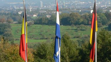 Detail of flags of Belgium, Netherlands and Germany from the tripoint ('Drielandepunt' in Dutch, 'Trois Frontières' in French, and 'Dreiländereck' in German), where the borders of the three countries meet. Forest and buildings of Aachen (Germany) in the background..Vaalserberg, Vaals, Limburg, The Netherlands, Europe.