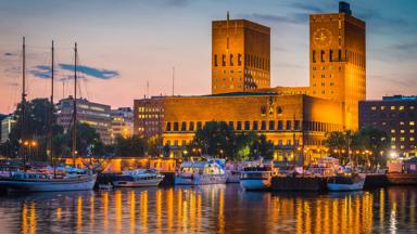 The iconic Functionalist towers of Oslo City Hall, Radhus, spotlit against the chrome blue dusk sky overlooking the harbour fjord and marinas of Aker Brygge, the popular leisure, dining and exclusive residential district in the heart of downtown Oslo, Norway's picturesque capital city. ProPhoto RGB profile for maximum color fidelity and gamut.