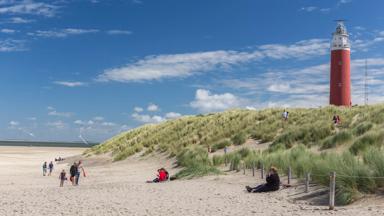 Several people enjoying the beach on the Dutch Wadden Island Texel on a sunny day in August, with lighthouse Eierlanden in the background. Texel, the Netherlands, August 2017.