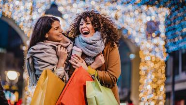 Two female friends are outdoors holding shopping bags
