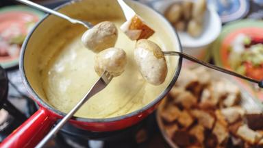The famous authentic Swiss cheese fondue served in an earthenware pot, with cubed breads and potatoes  dipping into rich melted cheese, landmark of Switzerland.