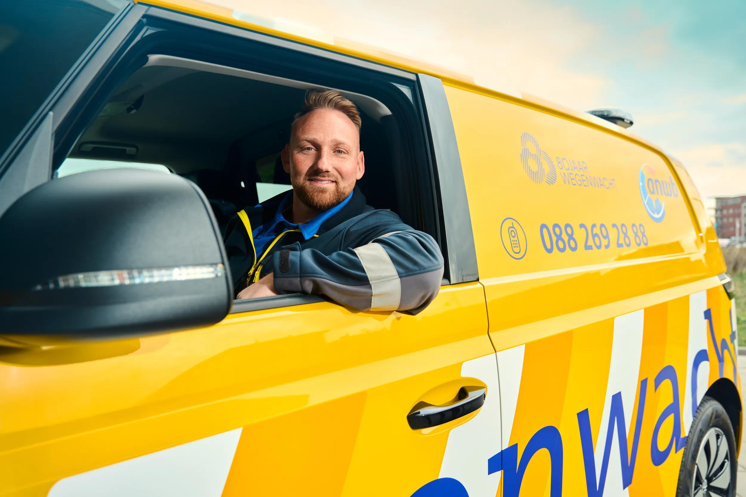 Wegenwacht monteur zittend achter het stuur in zijn bus met het raam open en glimlacht